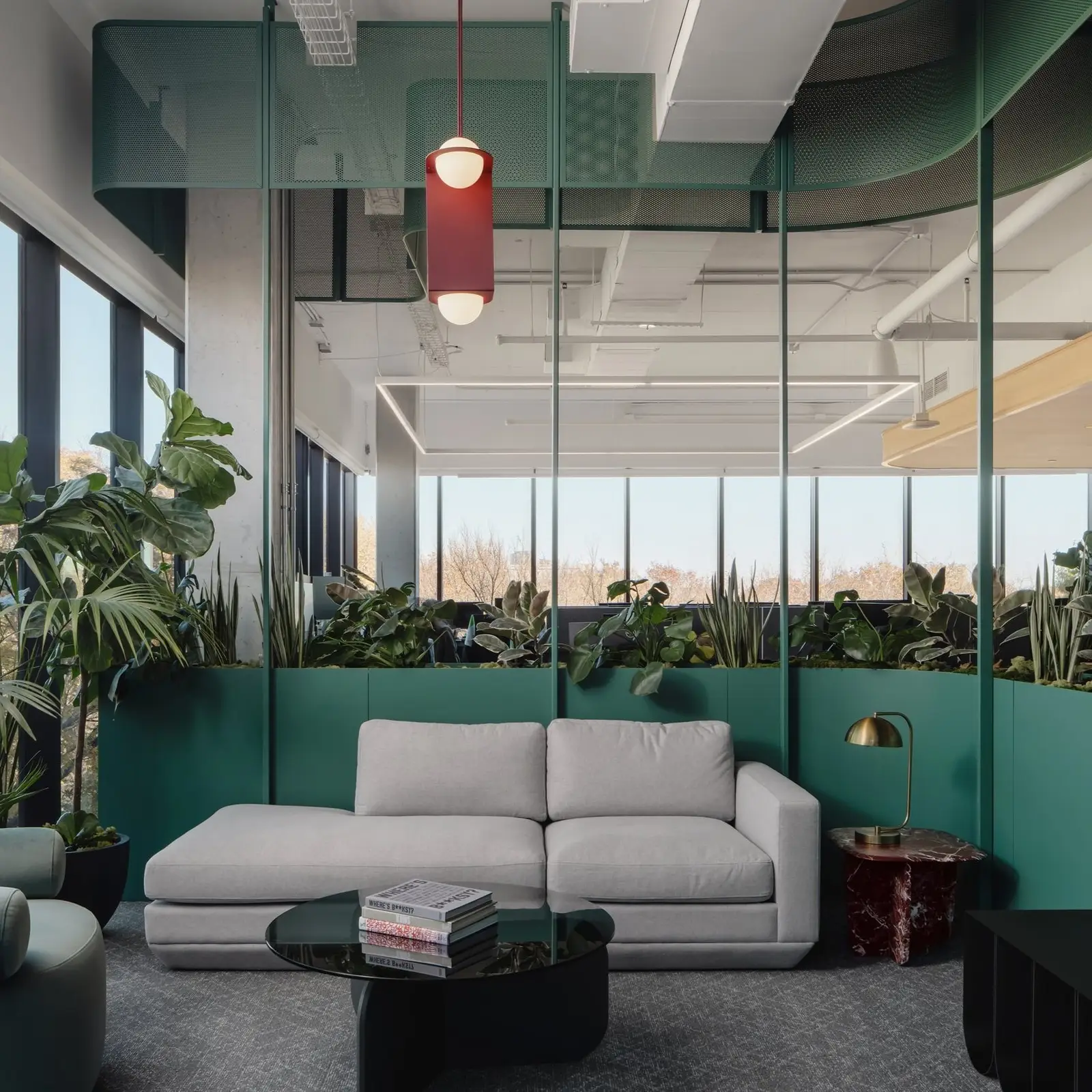 Office lounge with a gray sofa, teal planter wall and glass partitions