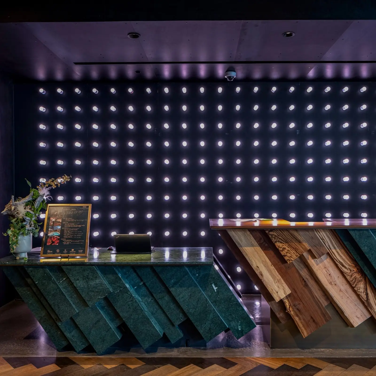 Hotel bar with angled teal and wood panels on the counter front and a wall of lights