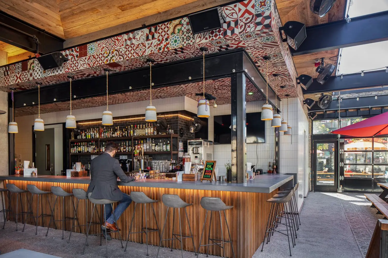 Arrive Hotel bar with a wood front, a patterned ceiling and stools