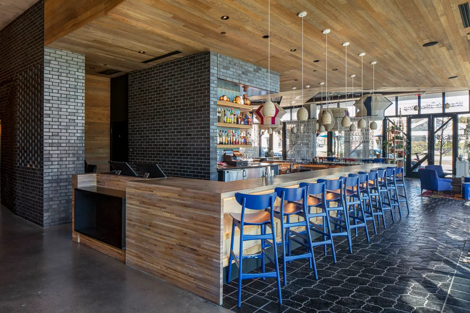 Arrive Hotel bar with a wood-front counter, a brick column and blue stools
