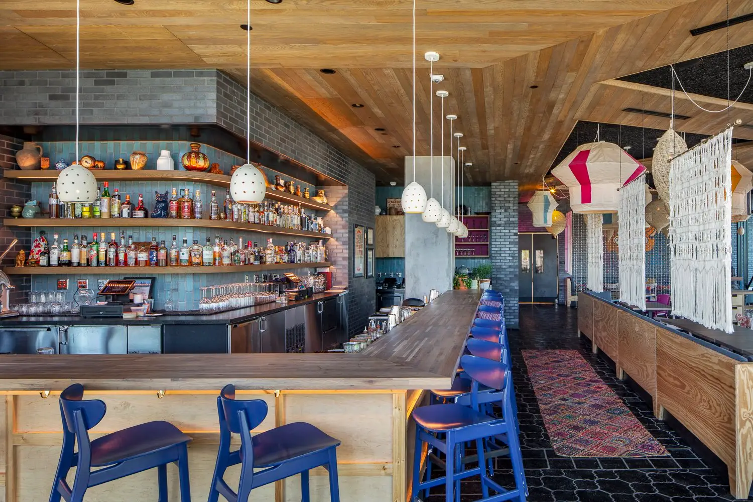 Arrive Hotel bar with wood shelves, blue stools and pendant lights