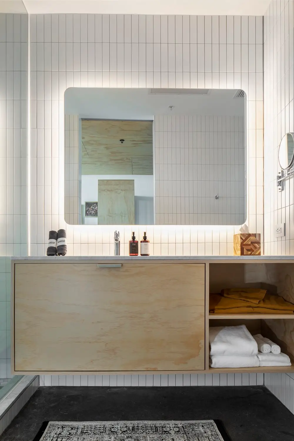 Arrive Hotel bathroom vanity with a wood-tone cabinet, backlit mirror and shelves