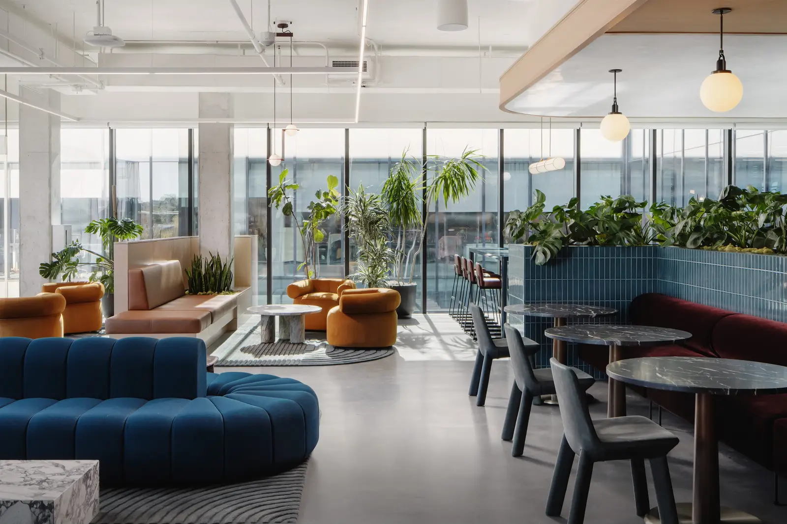 Atmosphere TV open lounge with blue curved seating, round tables and planters