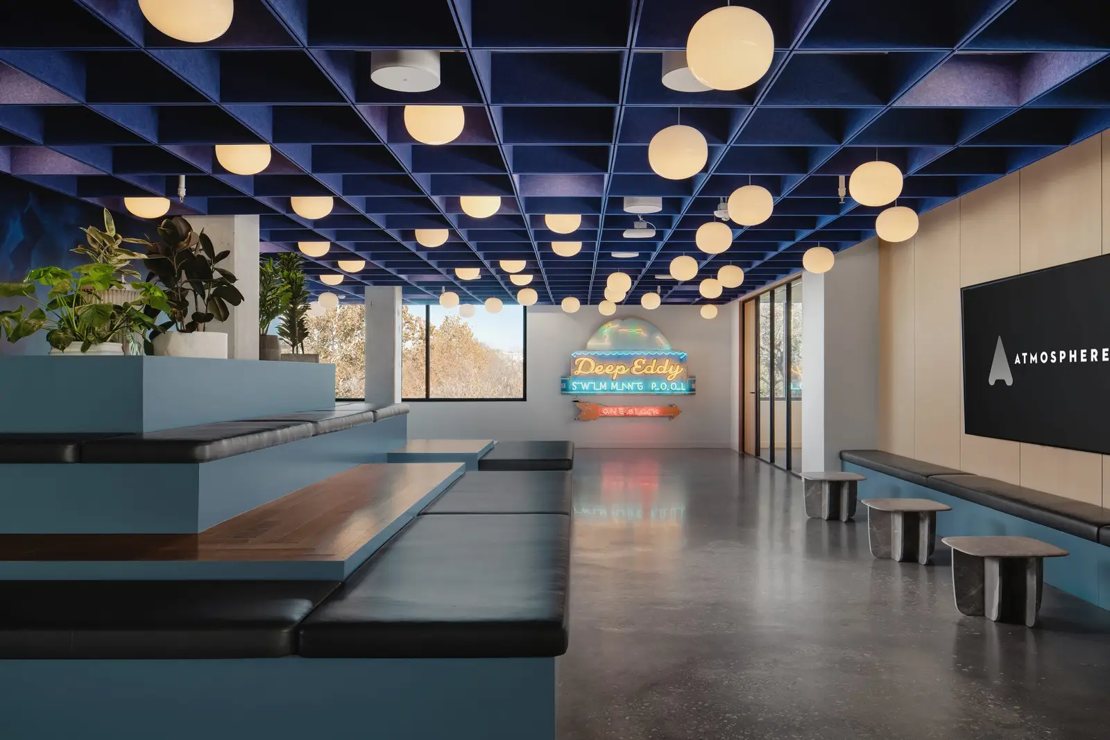Atmosphere TV tiered seating and a neon sign under a blue grid ceiling