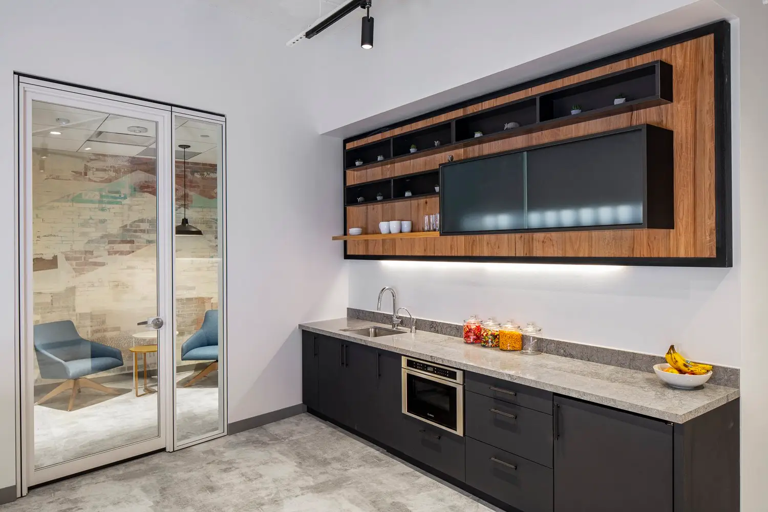 Boston Consulting Group kitchenette with dark cabinets and a wood-framed upper cabinet beside a glass door