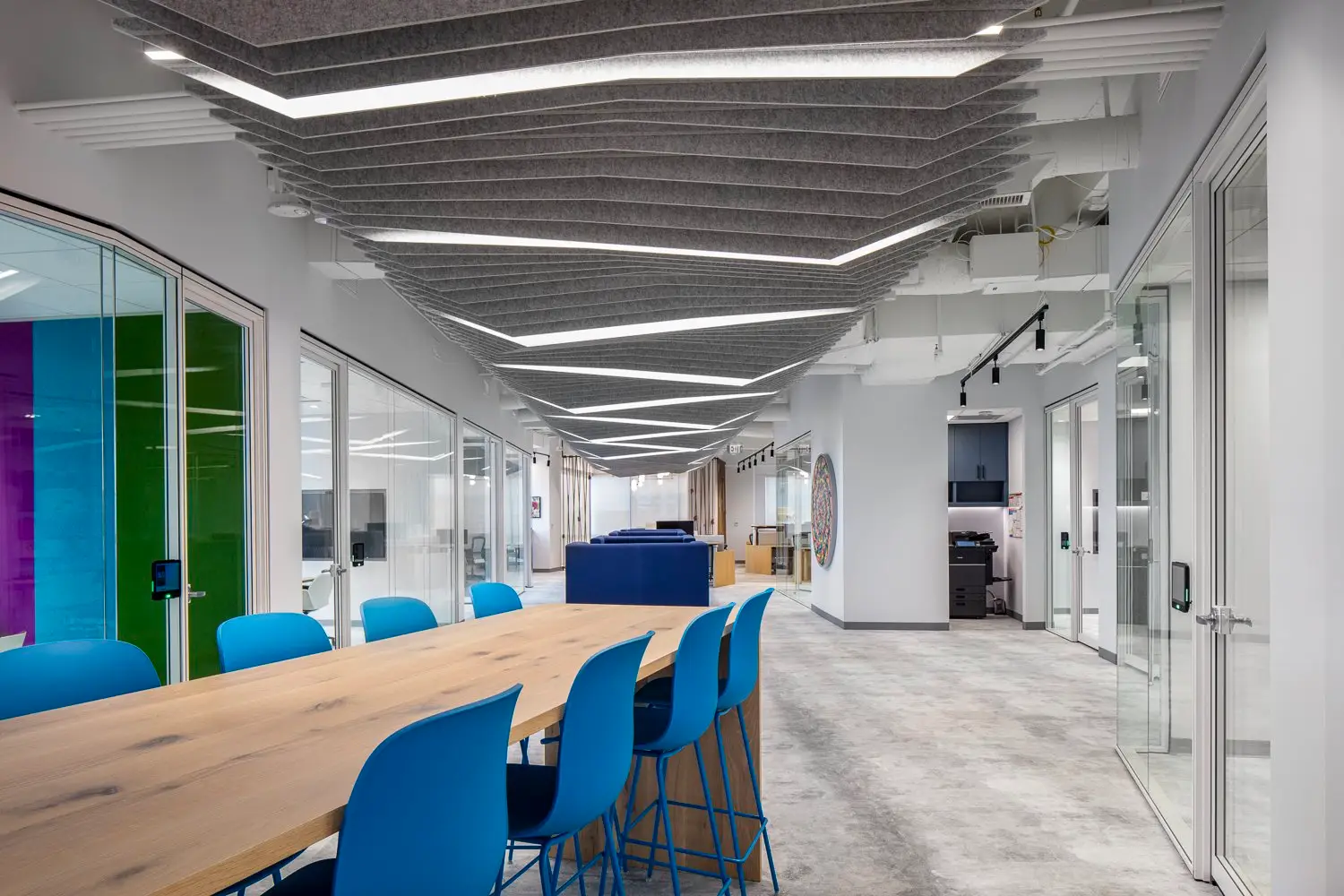 Boston Consulting Group long wood table with blue stools beside glass-walled offices