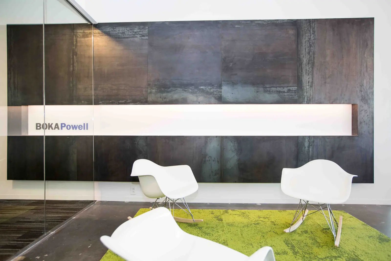 Boka Powell reception wall of dark metal panels with a lit sign and white chairs on a green rug