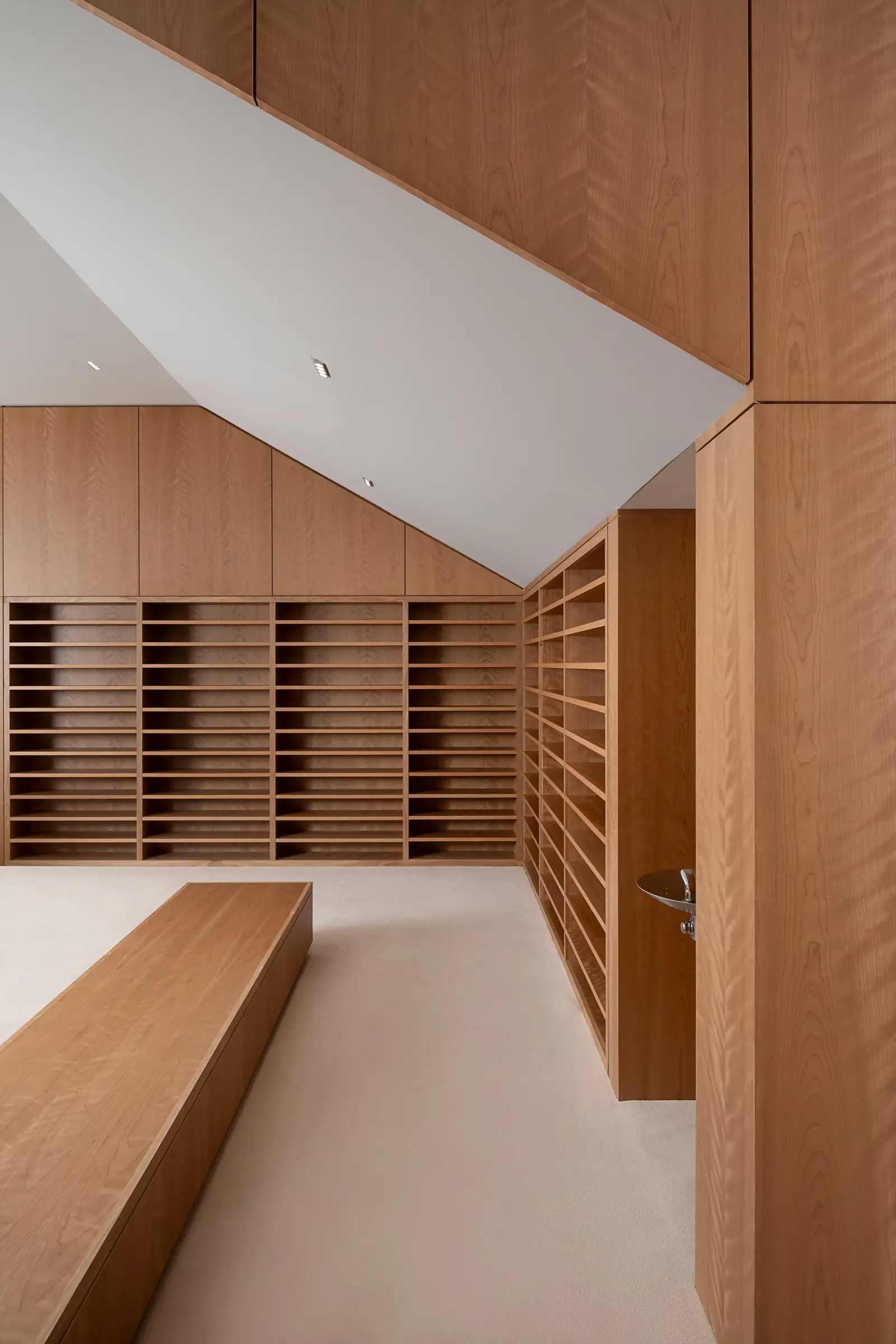 Ismaili Centre stair-side wood wall with slotted shelving and a bench
