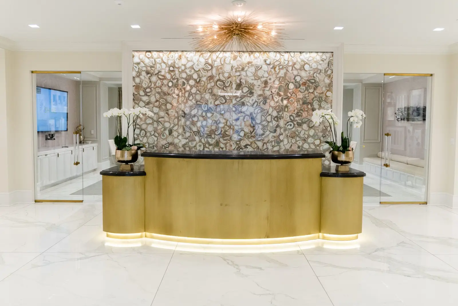 Kendra Scott reception desk with a gold-tone front and a mosaic wall
