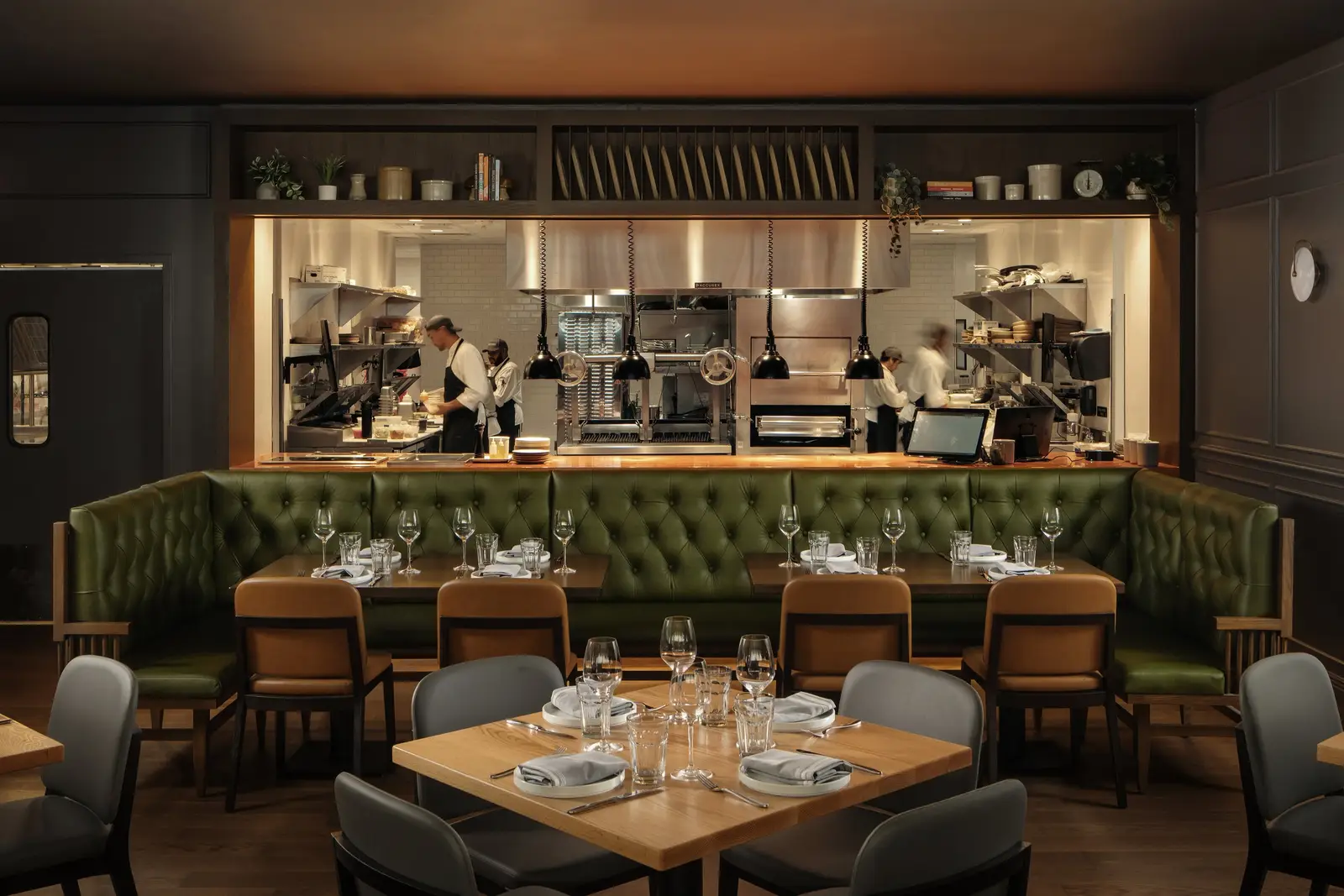 The Kitchen Bistro dining area with a green tufted banquette facing an open kitchen