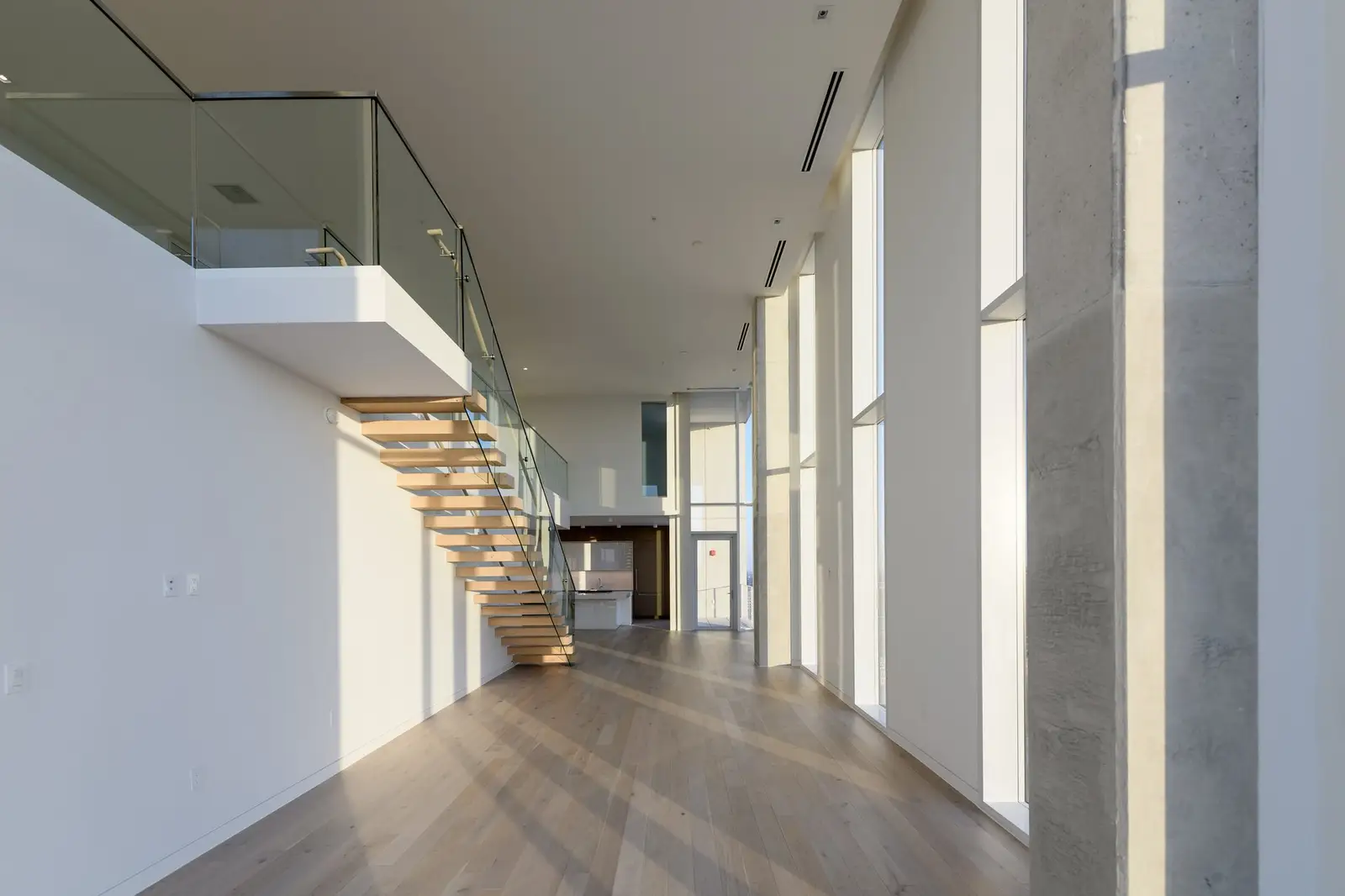 Linden Residences stair with wood treads and a glass guardrail in a tall space