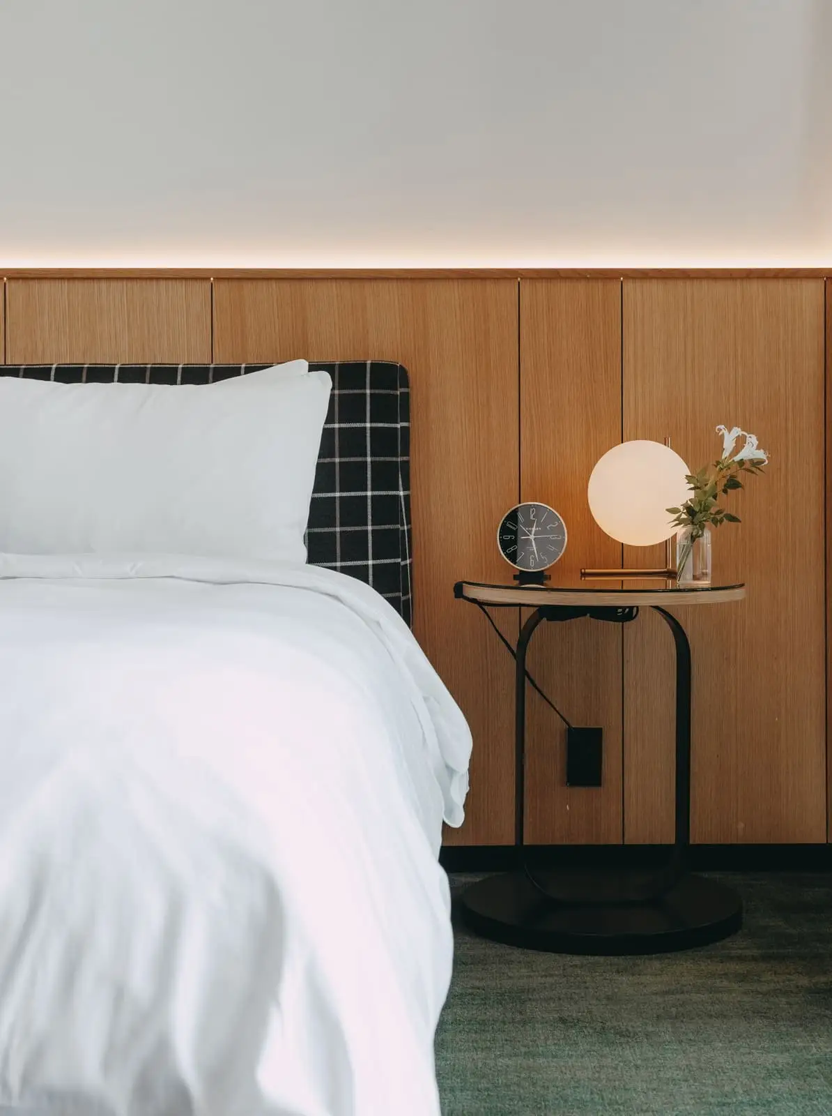 Loren Hotel bed and nightstand against a wood-paneled headboard wall