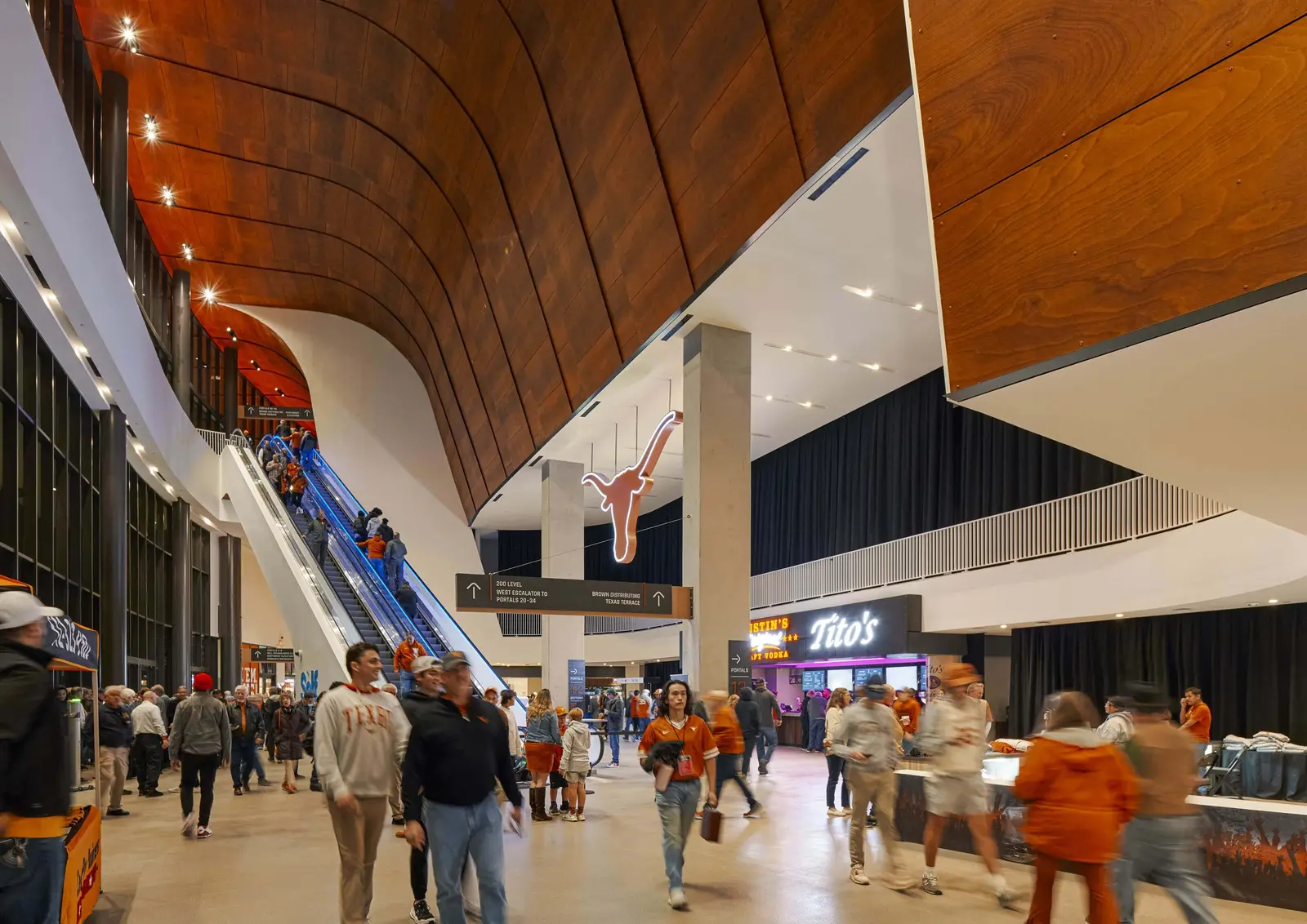 Moody Center concourse with a curved wood ceiling, escalator and crowd