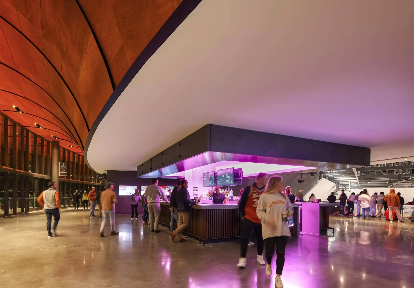 Moody Center concourse with a curved wood ceiling and a lit purple bar
