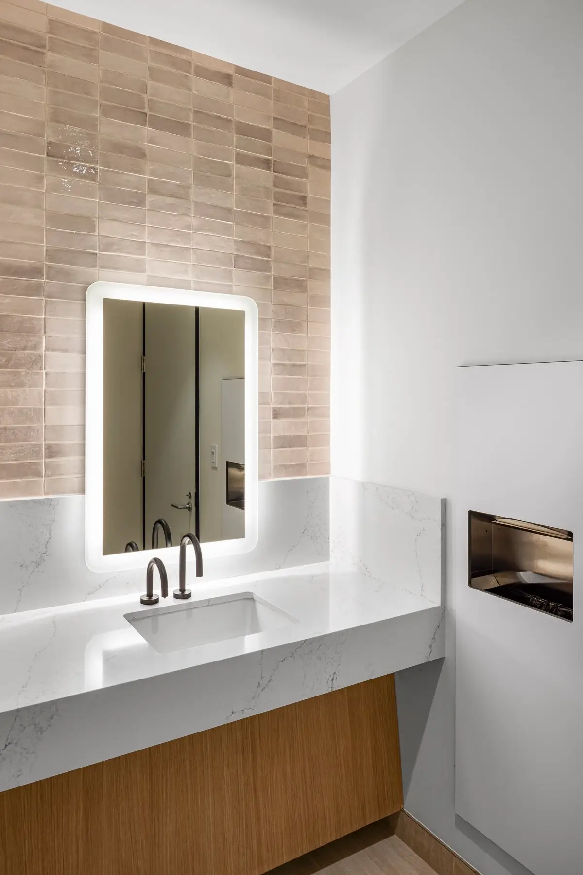Norton Rose Fulbright restroom vanity with a stone top, backlit mirror and tile wall