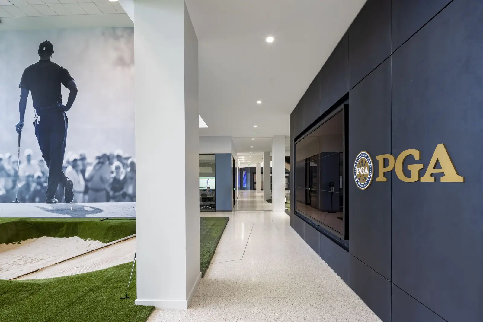 PGA of America corridor with a dark metal-clad wall and a PGA logo beside a golf mural