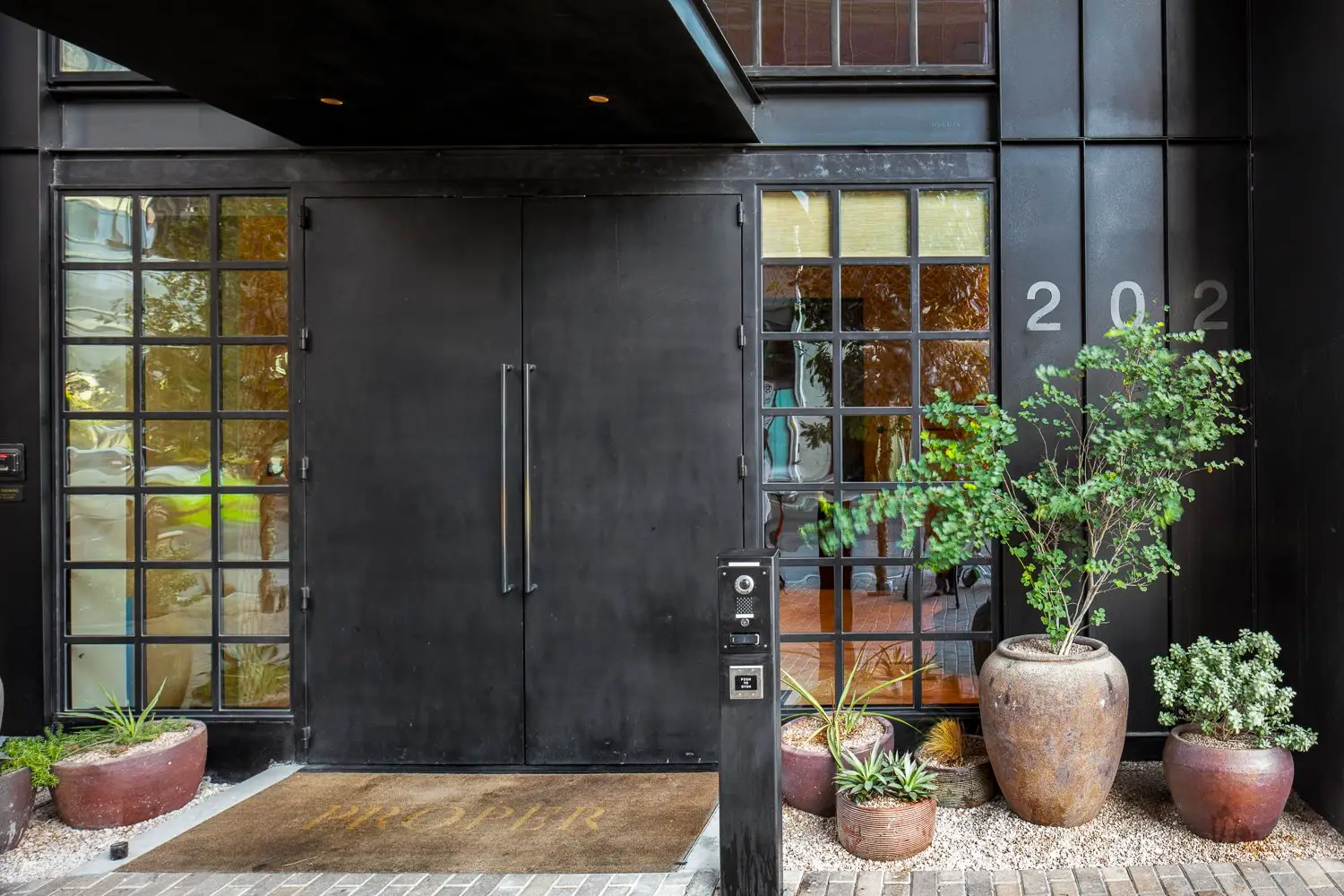 Austin Proper Hotel street entrance with a dark double door, black-framed windows and potted plants