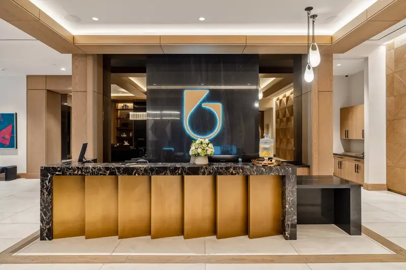 Sixth and Guadalupe lobby reception desk with a stone top and gold-tone fluted front below a lit logo wall