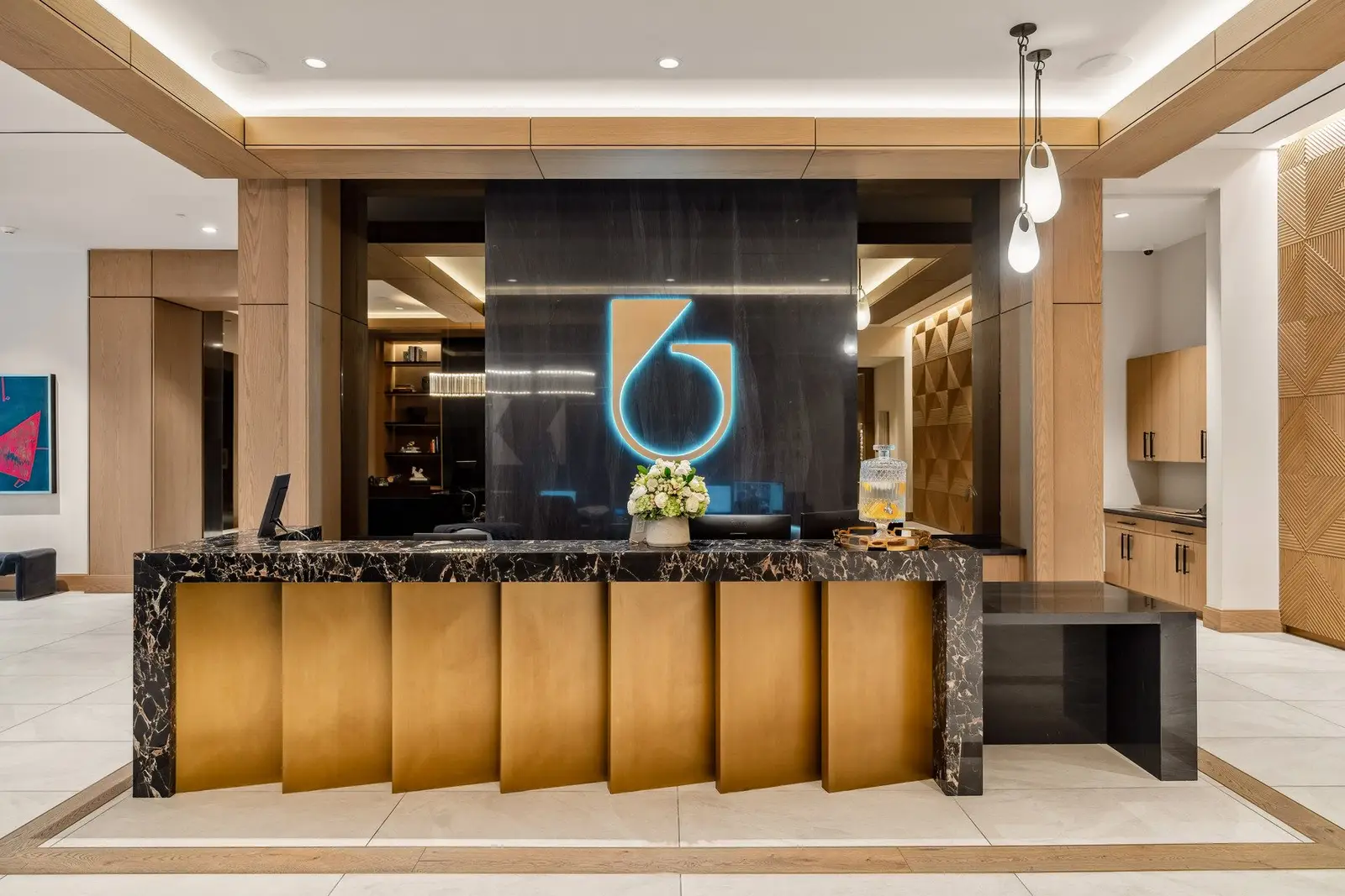 Sixth and Guadalupe lobby reception desk with a stone top and gold-tone fluted front below a lit logo wall