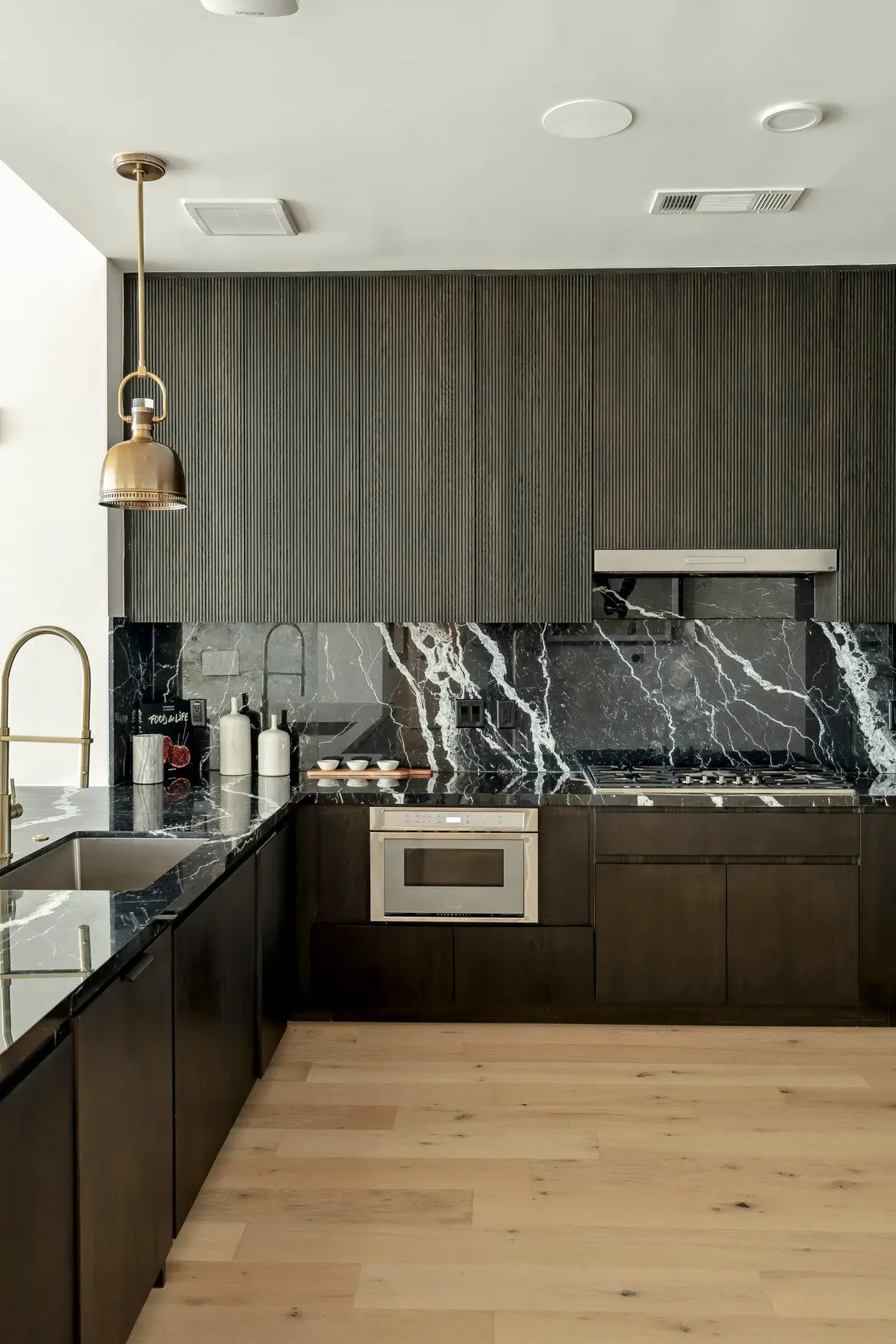 Sixth and Guadalupe kitchen with dark cabinets, a black marble backsplash and a pendant light