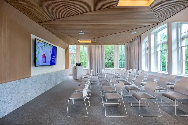 St. Edward's University presentation room with a faceted wood ceiling, stone wainscot and rows of white chairs