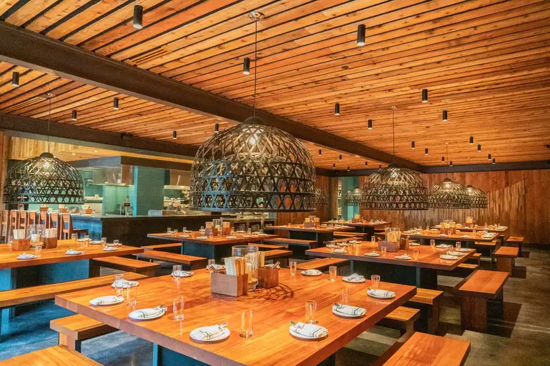 Sway Domain restaurant with a wood plank ceiling, communal wood tables and woven pendant lights