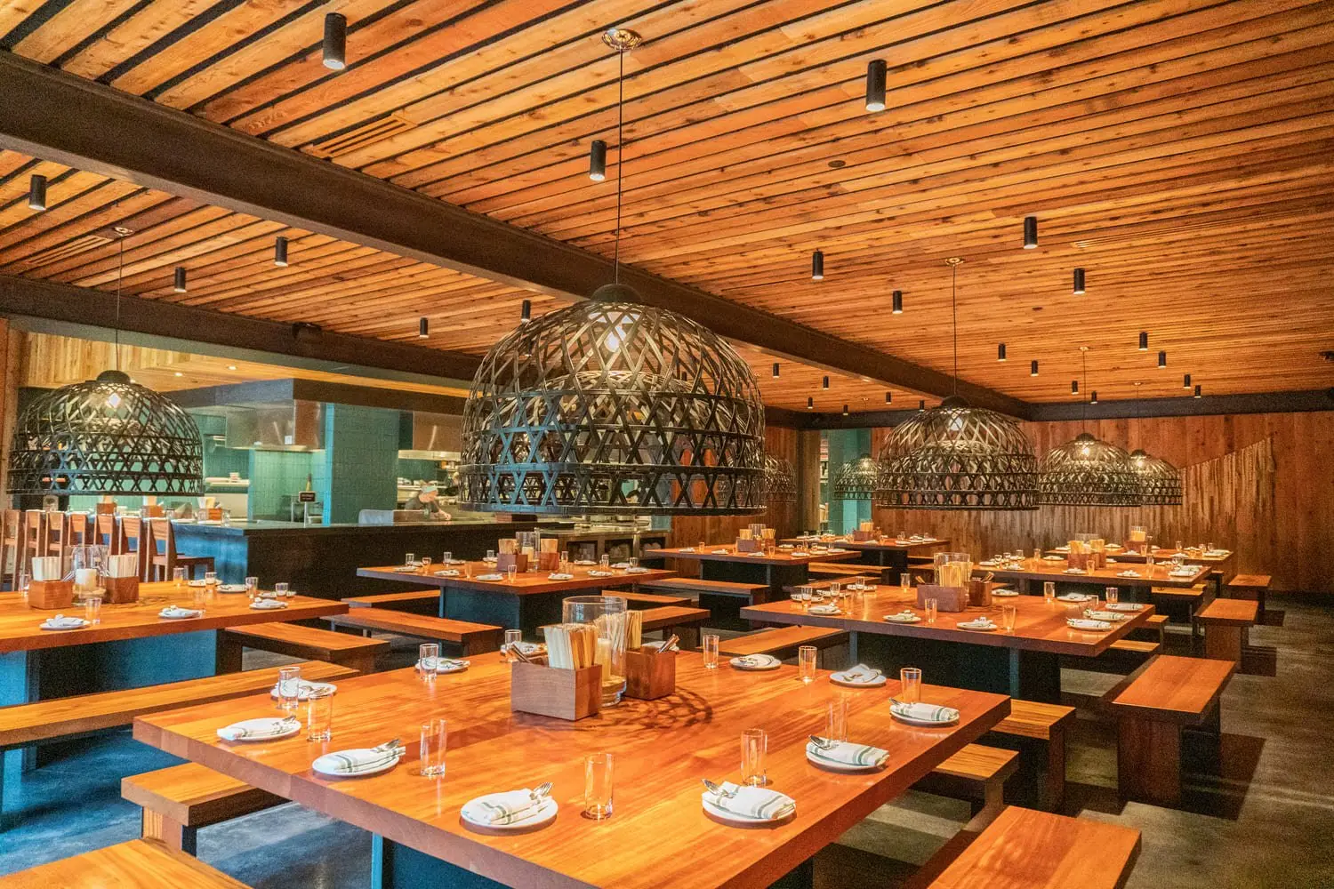 Sway Domain restaurant with a wood plank ceiling, communal wood tables and woven pendant lights