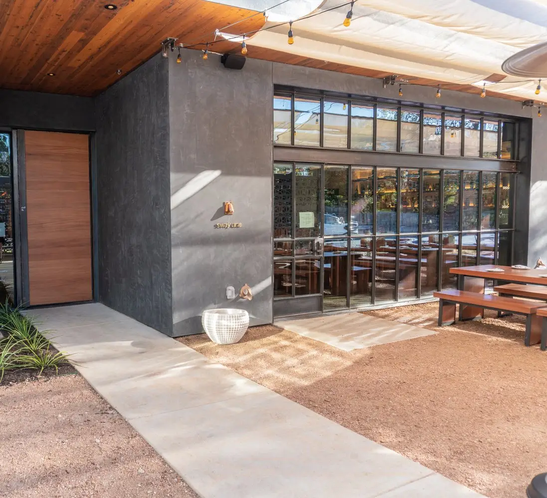 Sway Bee Caves restaurant entrance with a wood door, a dark wall and glass doors to a patio