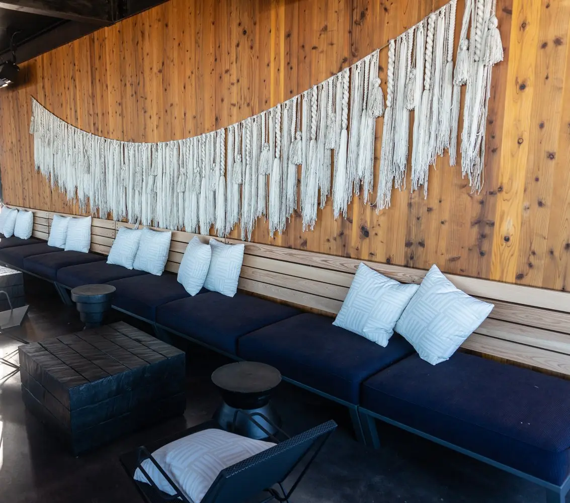Sway Bee Caves booth seating with navy cushions under a wood wall with a macrame hanging