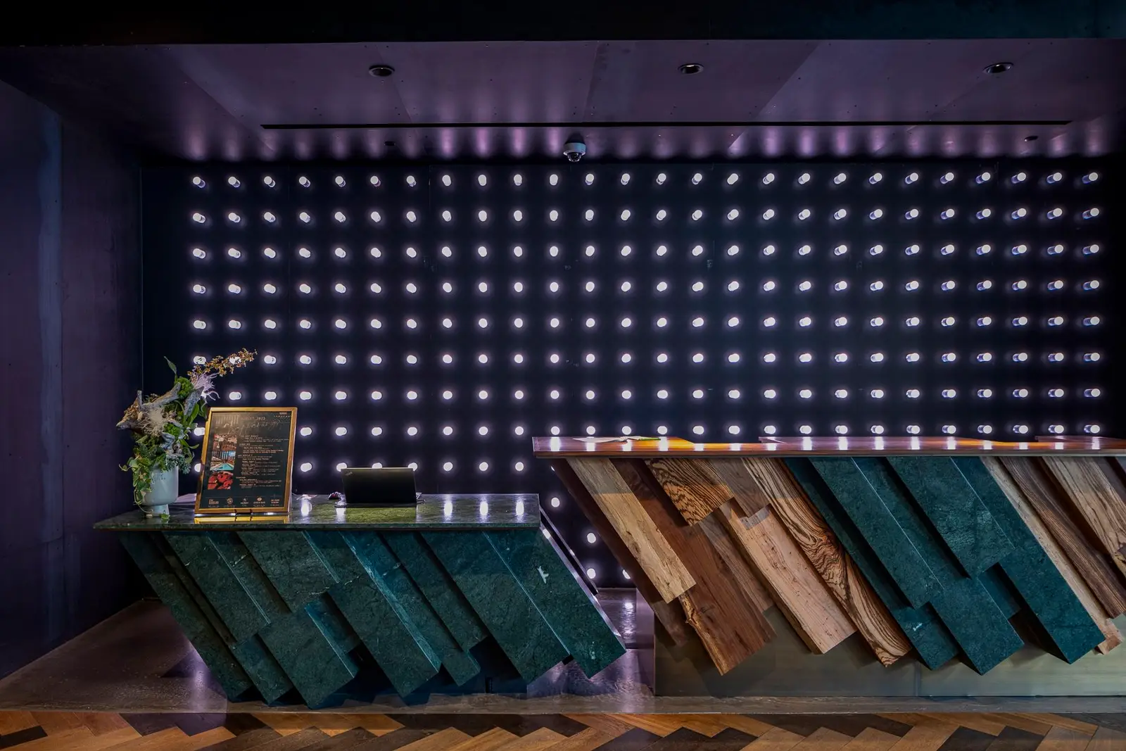 Thompson Hotel hotel lobby reception counter of angled wood and teal panels before a wall of lights