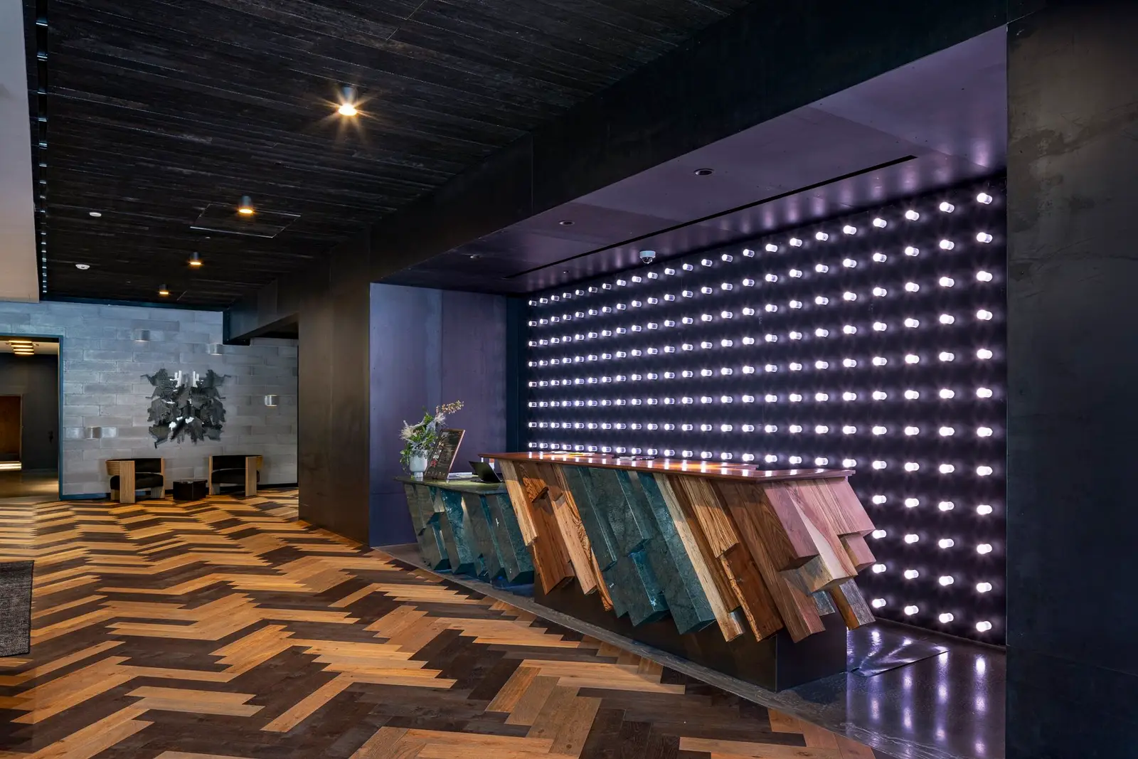 Thompson Hotel lobby with a herringbone wood floor and a lit wall behind an angled panel counter