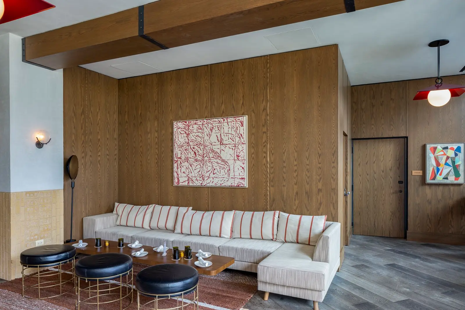 Thompson Hotel lounge with a wood-paneled wall, sectional sofa and round stools