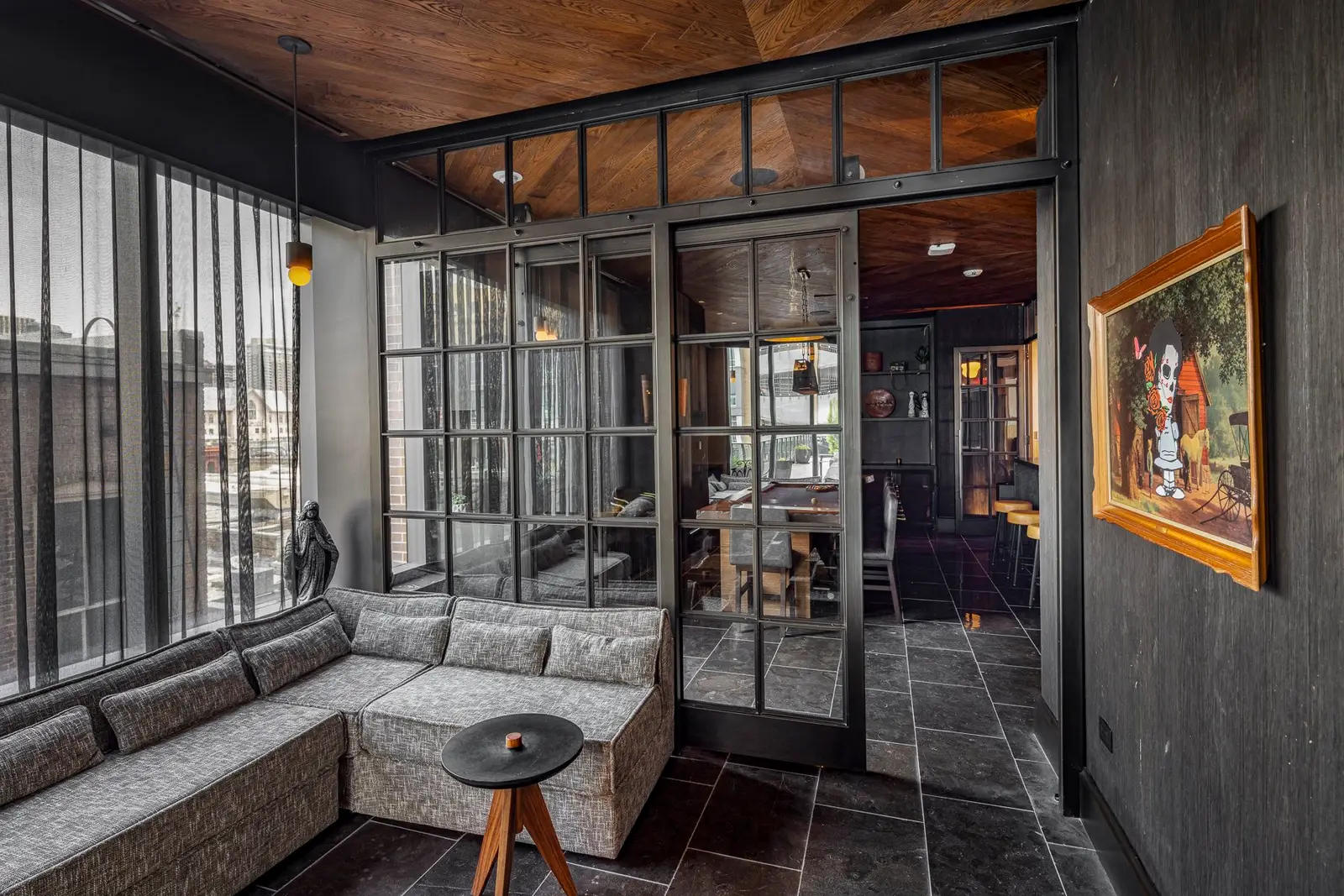 Thompson Hotel lounge with a gray banquette, black-framed glass doors and a framed painting