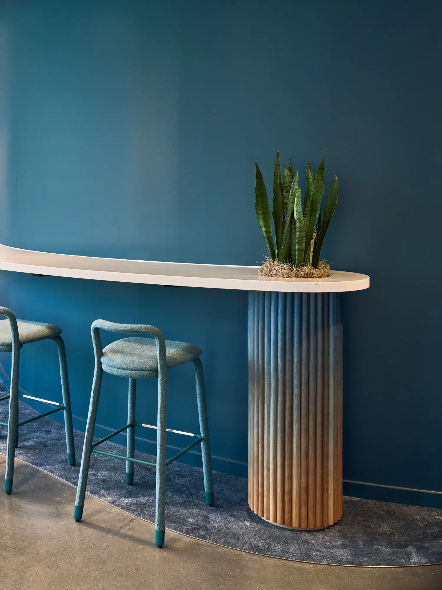 TikTok curved counter ledge on a fluted column with teal stools against a dark blue wall