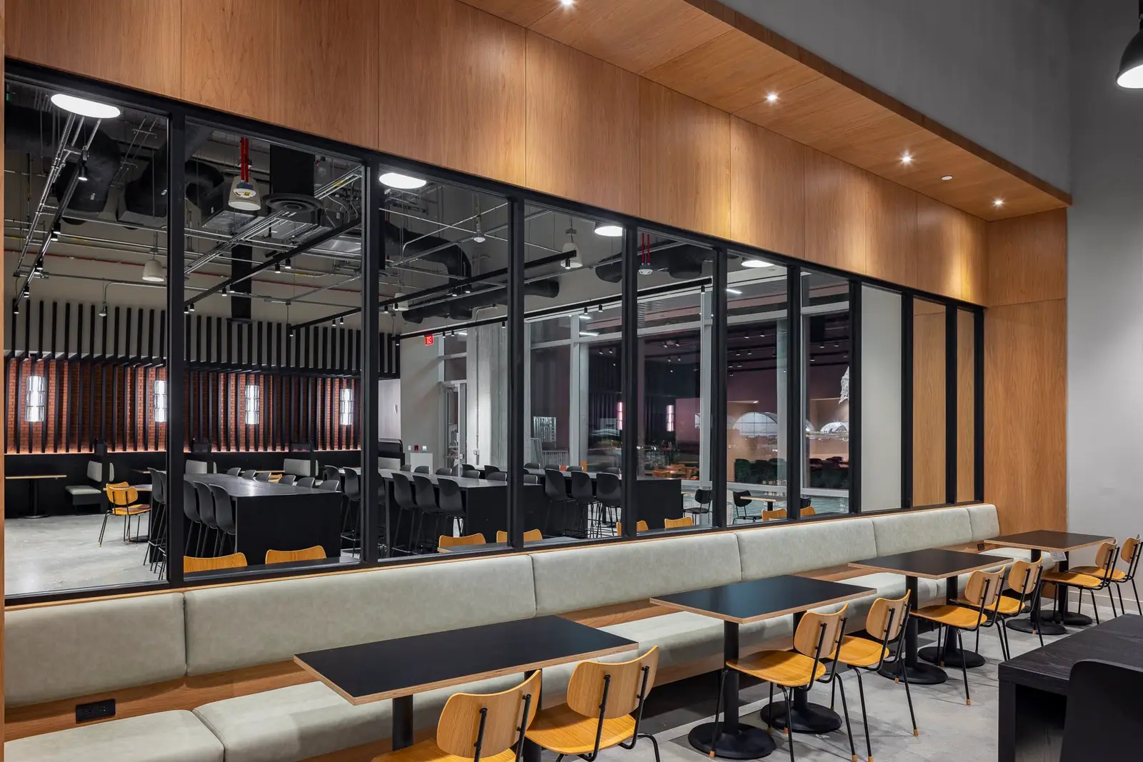 Undisclosed Project dining hall with a wood soffit, black-framed glass wall and banquette seating
