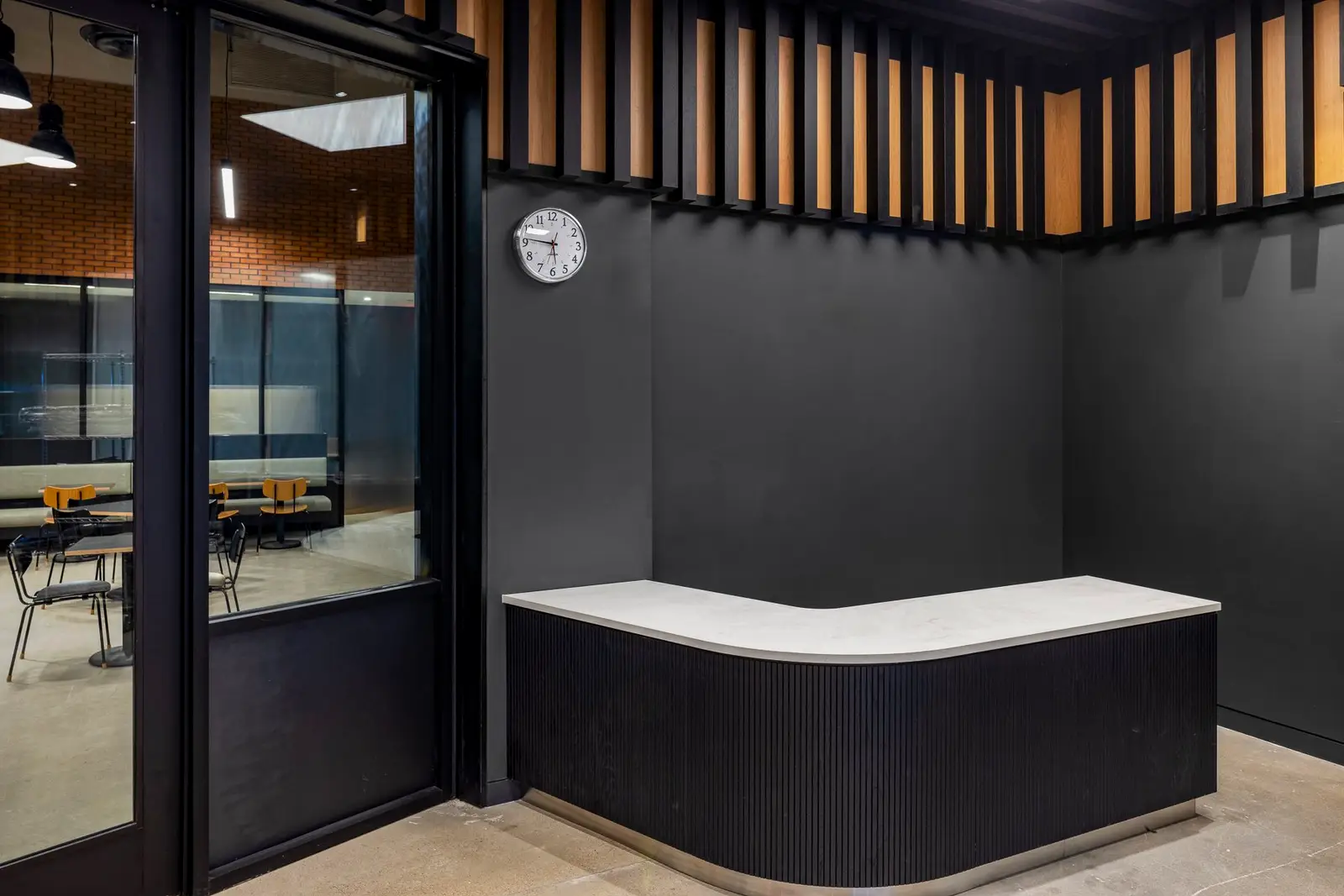 Undisclosed Project black curved reception counter with a white top beside a glass wall