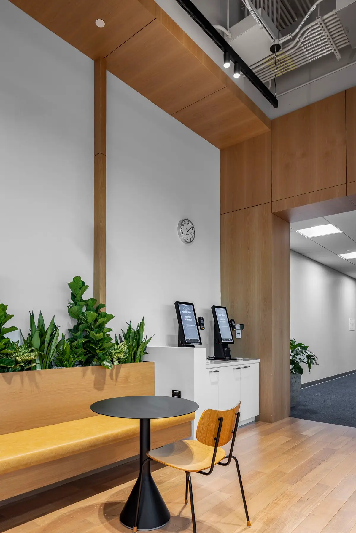 Undisclosed Project seating nook with plants and check-in kiosks under a wood-paneled ceiling