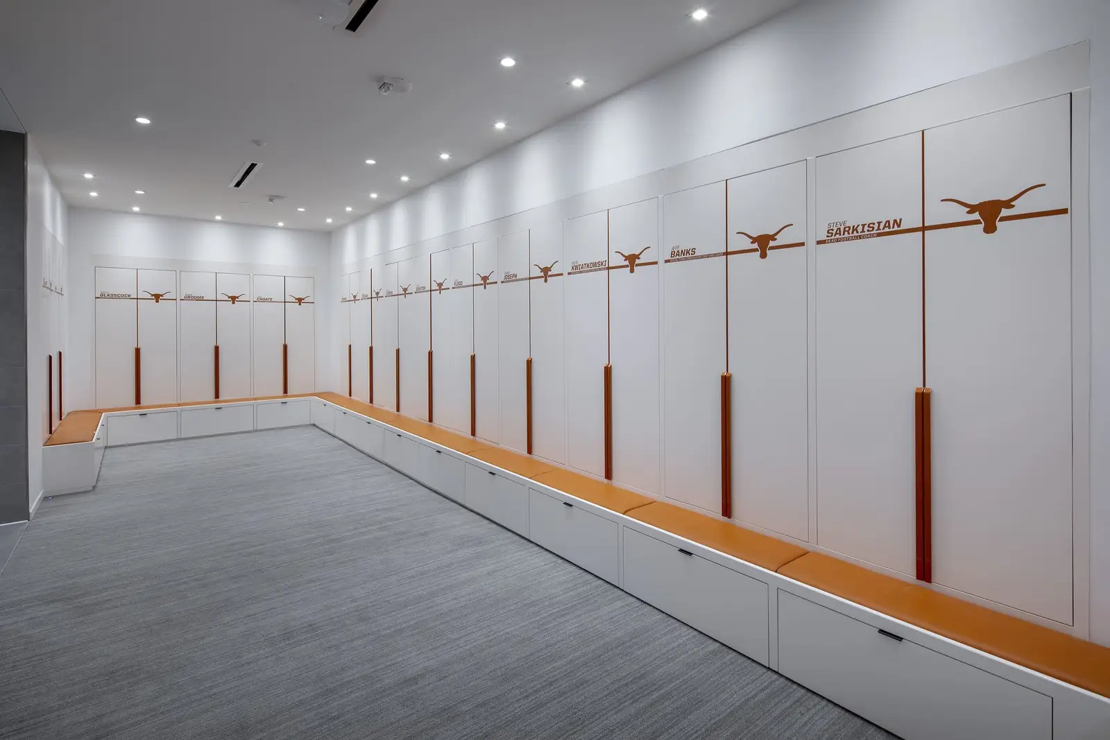 University of Texas South End Zone locker room with white lockers and wood benches marked with Longhorn logos