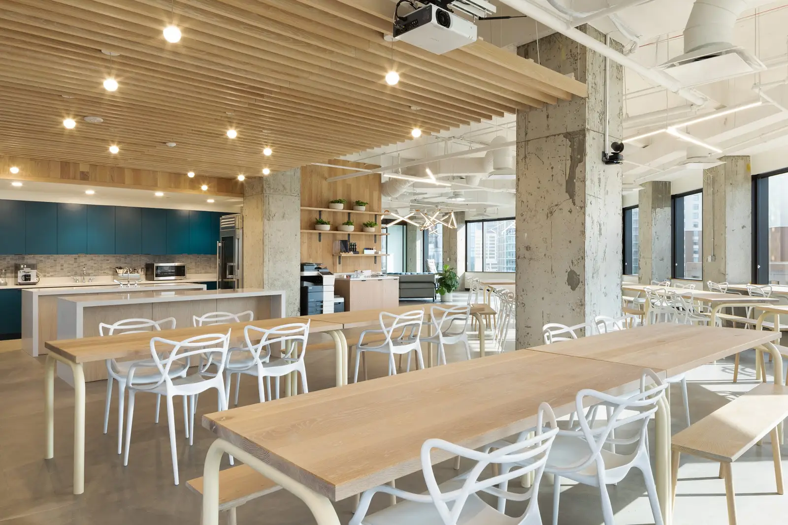 Workrise (formerly Rigup) break area with long wood tables, white chairs and a wood slat ceiling